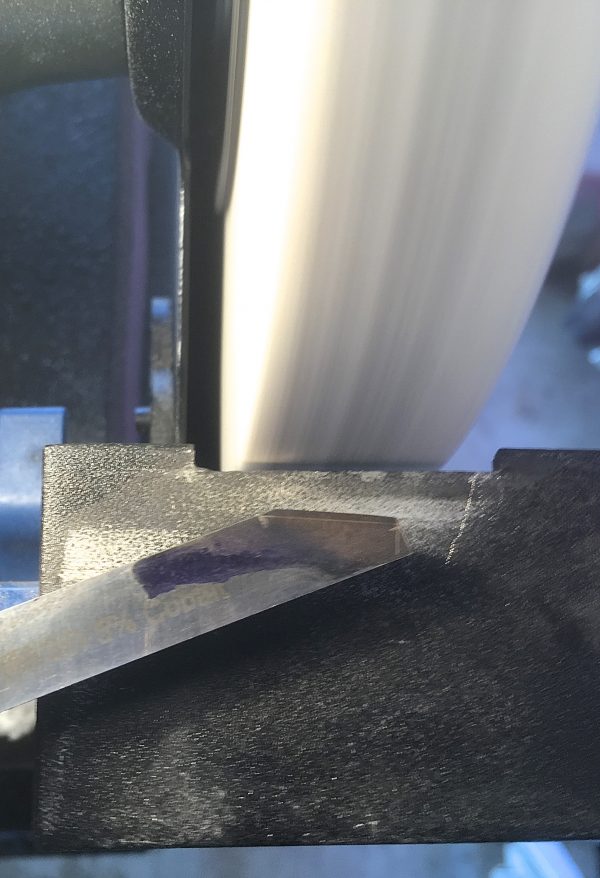 Holding the bit flat against the tool rest and sliding it back and forth on the wheel, cut the long side first. This will go quickly with the practice mild steel, but will seem to take forever with HSS. Be patient and work on deadening your heat nerves.